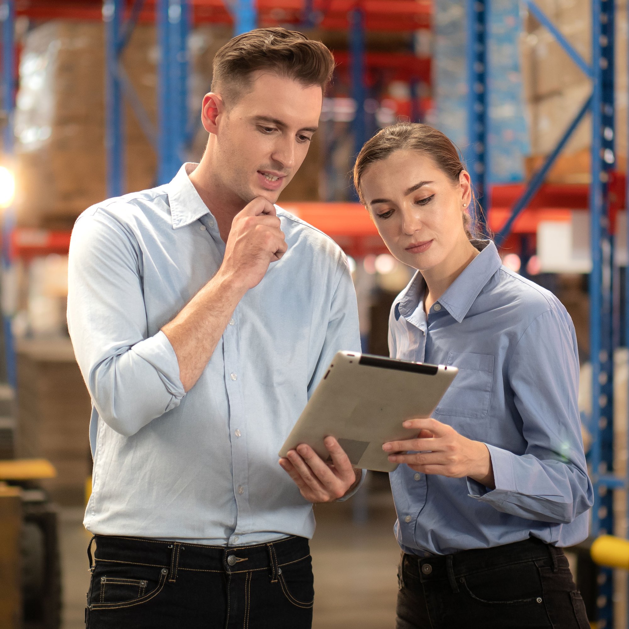 Two contract auditors reviewing complex supplier agreement terms on a tablet in a warehouse setting.
