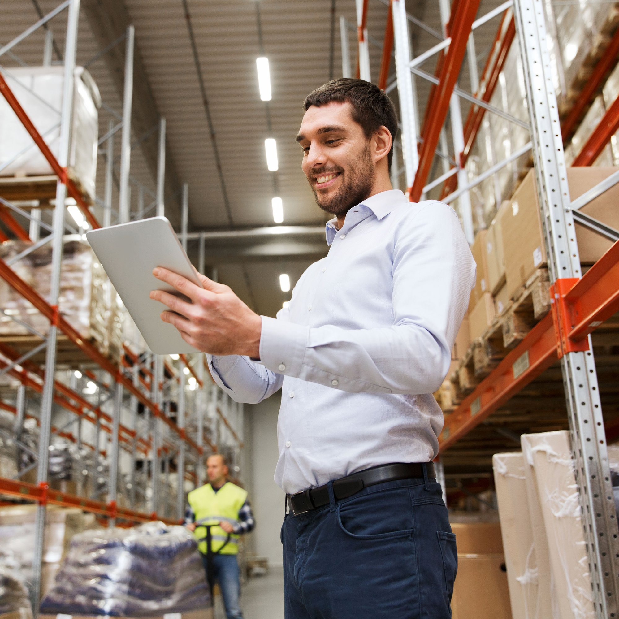 Male AP employee using a tablet in warehouse to identify duplicate payments during cost recovery audit.
