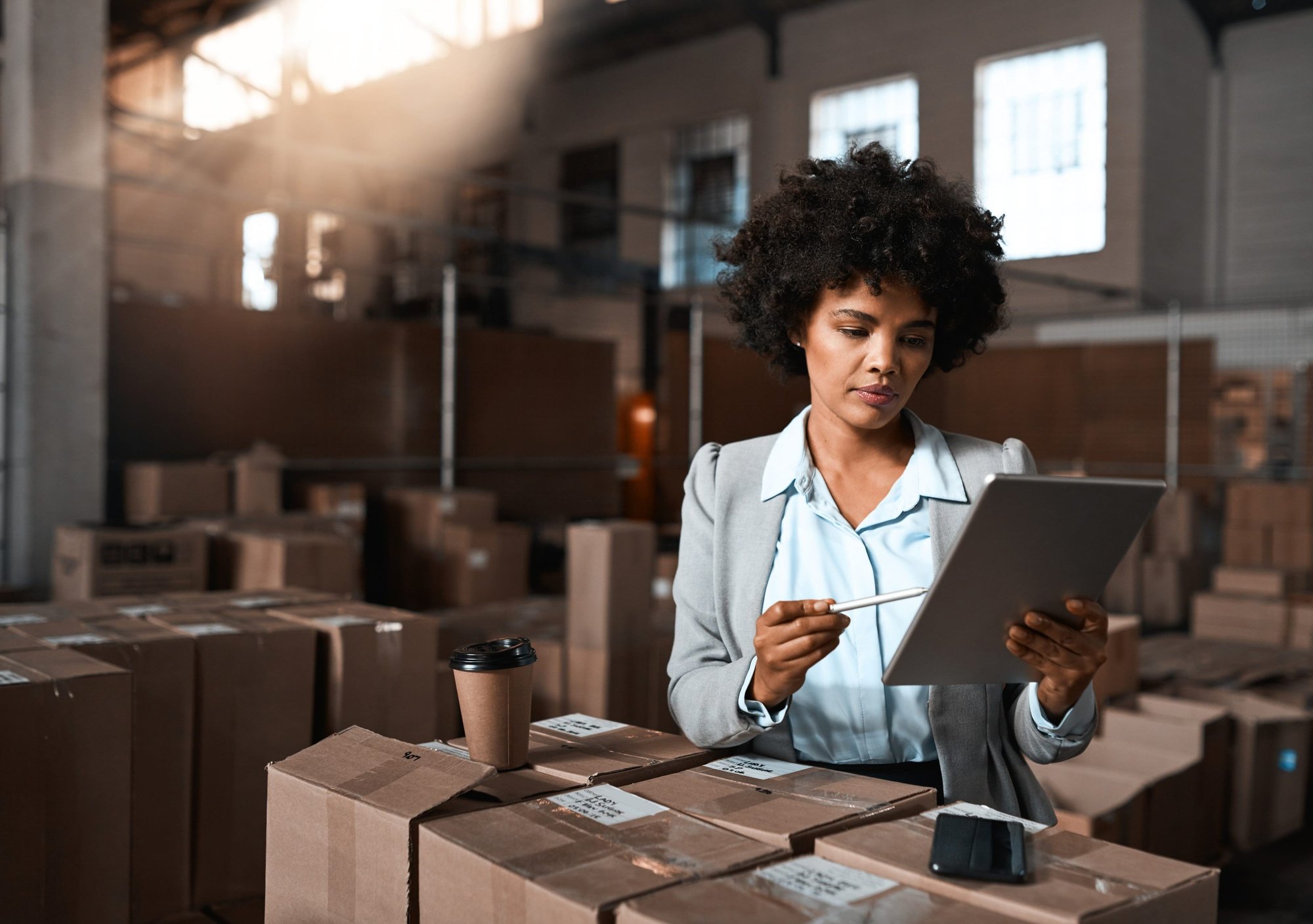 Female retail audit professional reviewing inventory on tablet in warehouse.